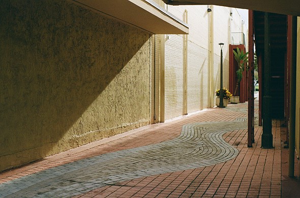 sunshine pours into an alley with a blue brck river surrounded by red bricks and yellow walls