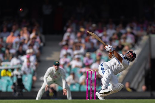 a cricket player swings with stands behind him