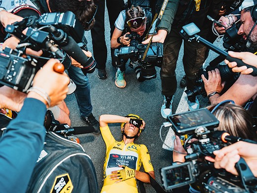 a cyclist is collapsed on the ground with a crowd of cameras hovering over her