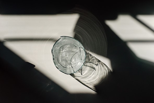 a glass filled with broken shards of glass sits amidst dramatic shadows and light