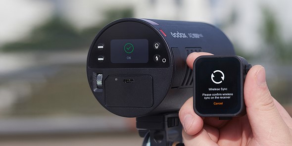 a hand holds a transmitter in front of a godox flash