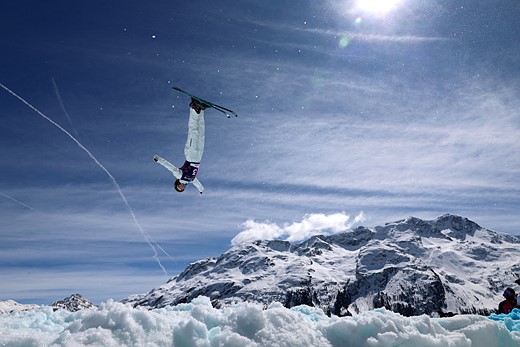 a skiier is suspended upside down with snowy mountains behind