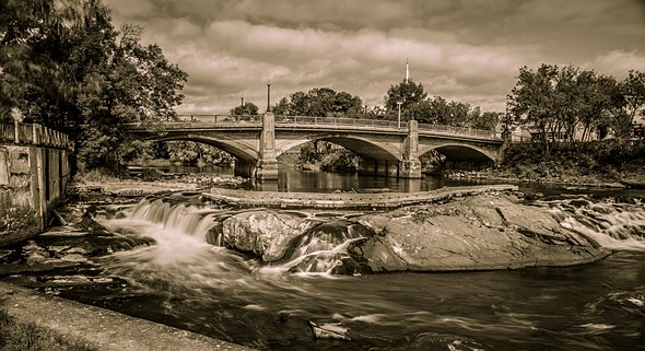an old bridge extends over a river with small waterfall