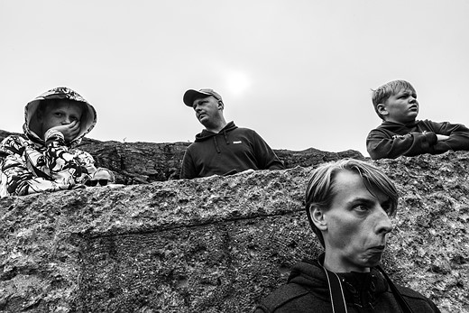 Black and white photo of four people partially hidden behind a rough concrete wall