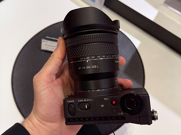 a hand holds a small camera with lens over a display table 1