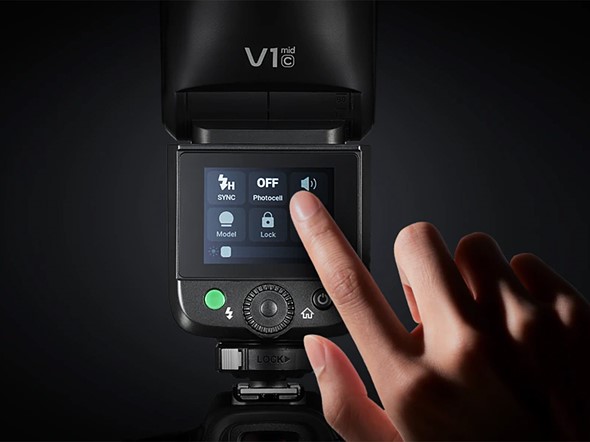 a hand points to a touchscreen on a black flash unit with a black background