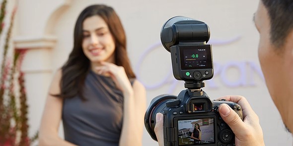 a person holds a camera with a flash on it while a woman poses