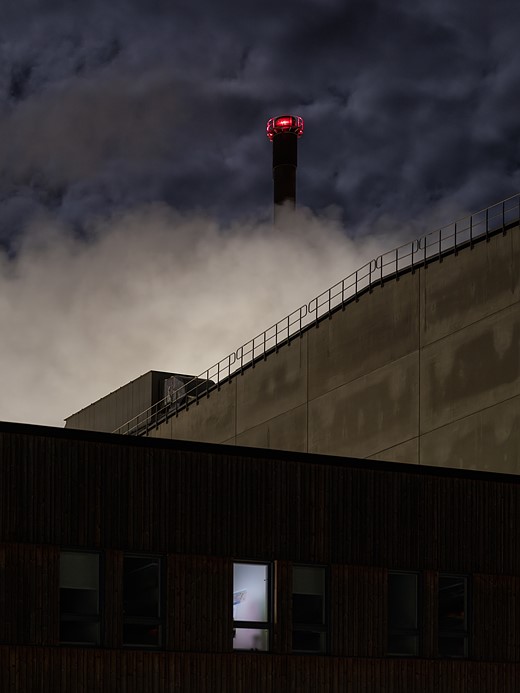 red lights at the top of a tower glow with dense clouds around it and a concrete building below