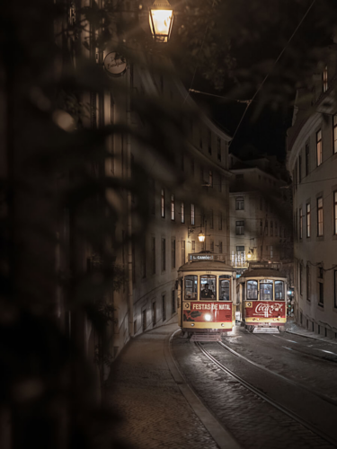 Two illuminated trams traveling through a narrow city street at night, composed using the rule of thirds in photography with leading lines and depth.