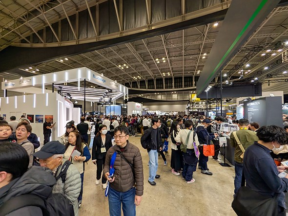 a crowd of people fills a large expo hall with booths for different companies