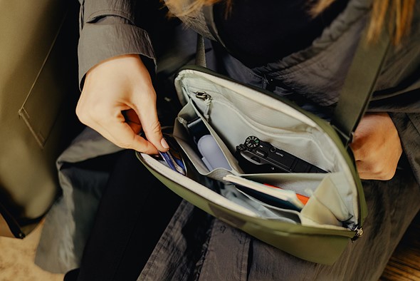 a hand pulls something out of a small green sling set on a persons lap