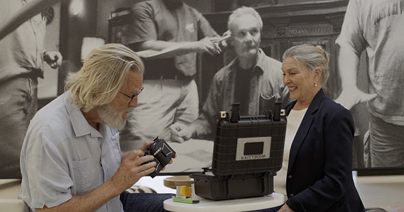 a man holds a camera while a woman sits across a table from him smiling