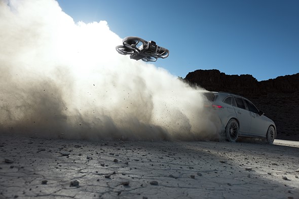 a small drone flies behind a car kicking up a cloud of dust and rocks