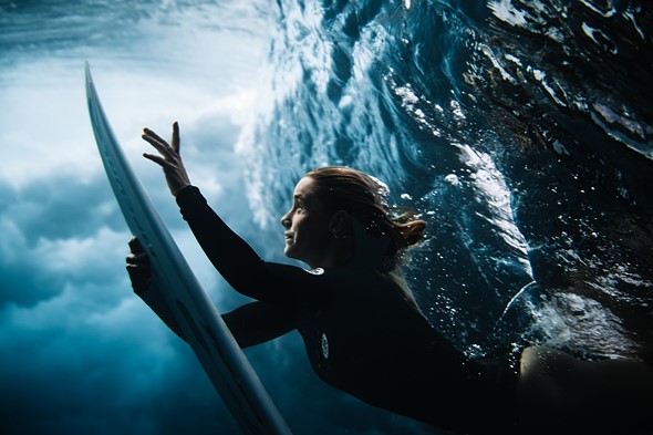a woman duck dives beneath a wave with her surf board