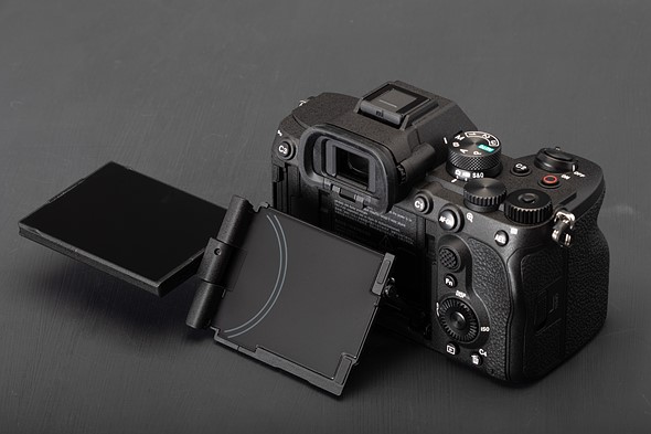 a camera sits With its rear display extended on a black surface
