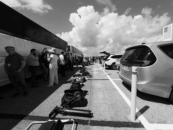 people line up against a line of buses with bags of gear in front
