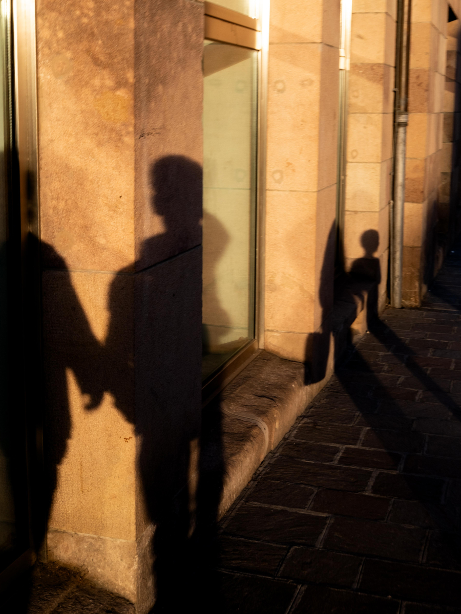 Shadow shapes photography of people holding hands cast on a sunlit wall, with long dramatic shadows stretching across the street in warm golden light.