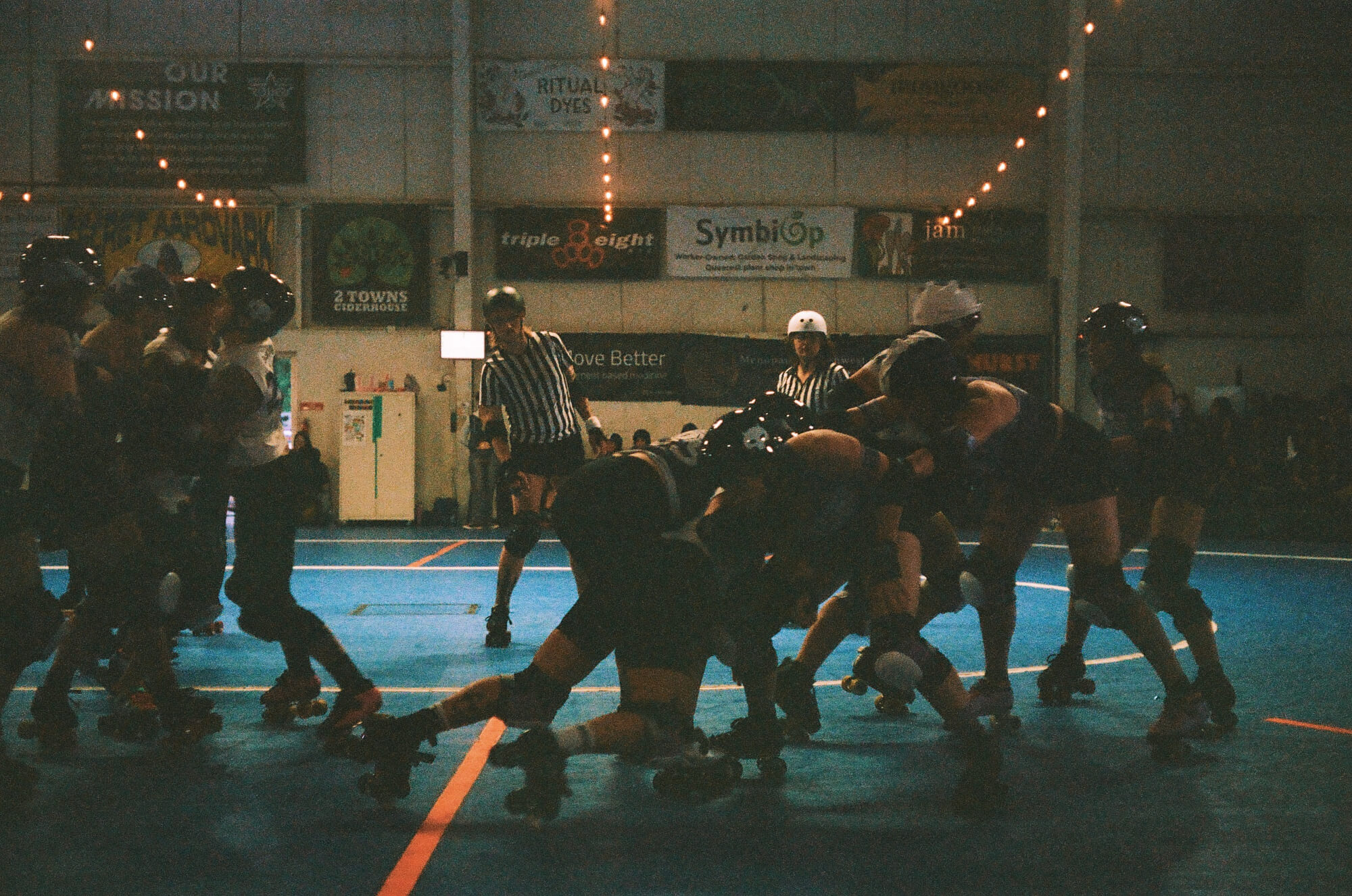 Roller derby players in motion under warm indoor lighting, captured in a gritty, cinematic style inspired by Mikey Rogers.