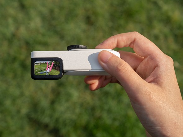 a hand holds a tiny white camera over blurred grass