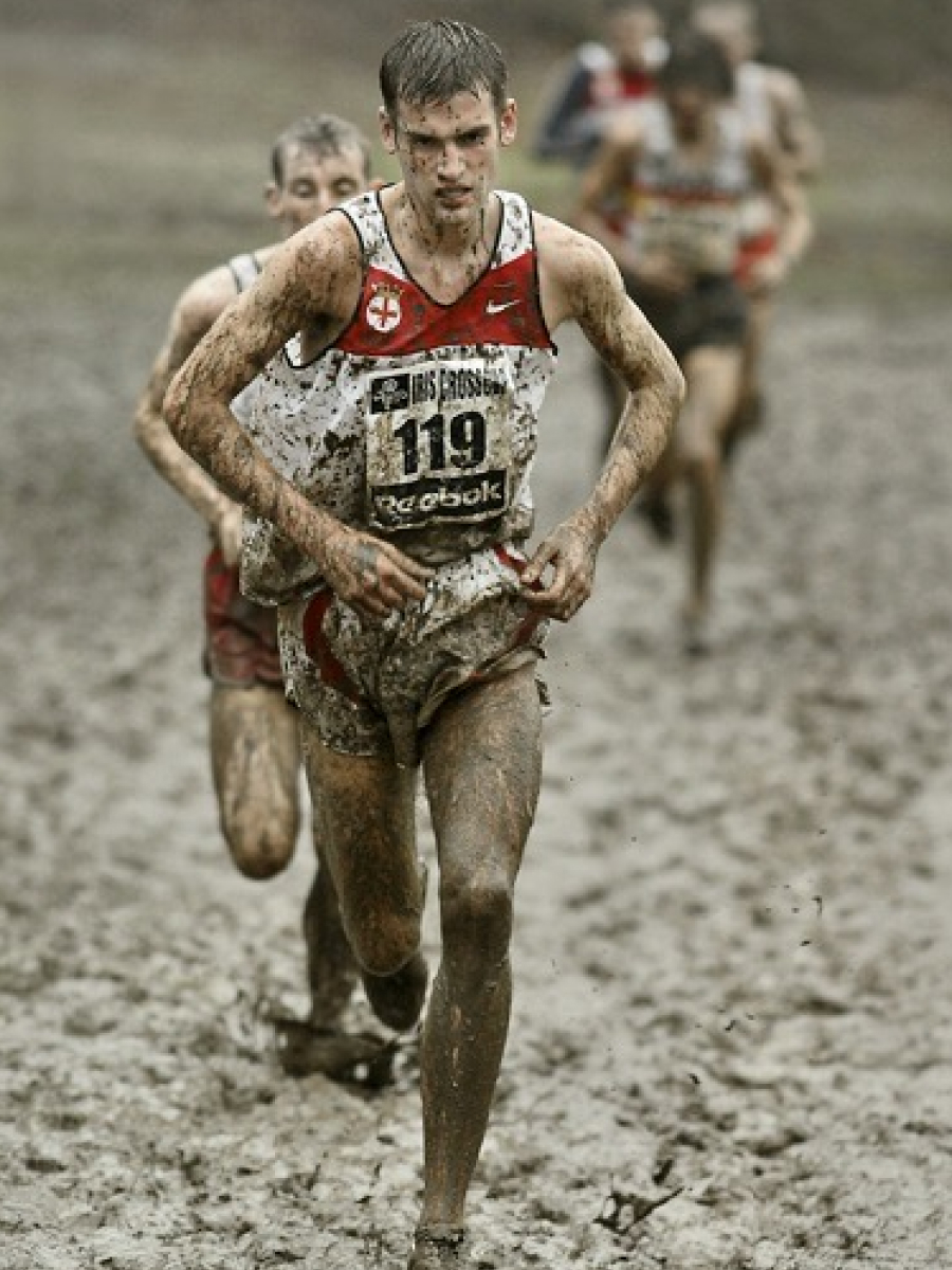 Muddy cross-country runner sprinting through wet terrain, frozen mid-stride using fast shutter speed photography.