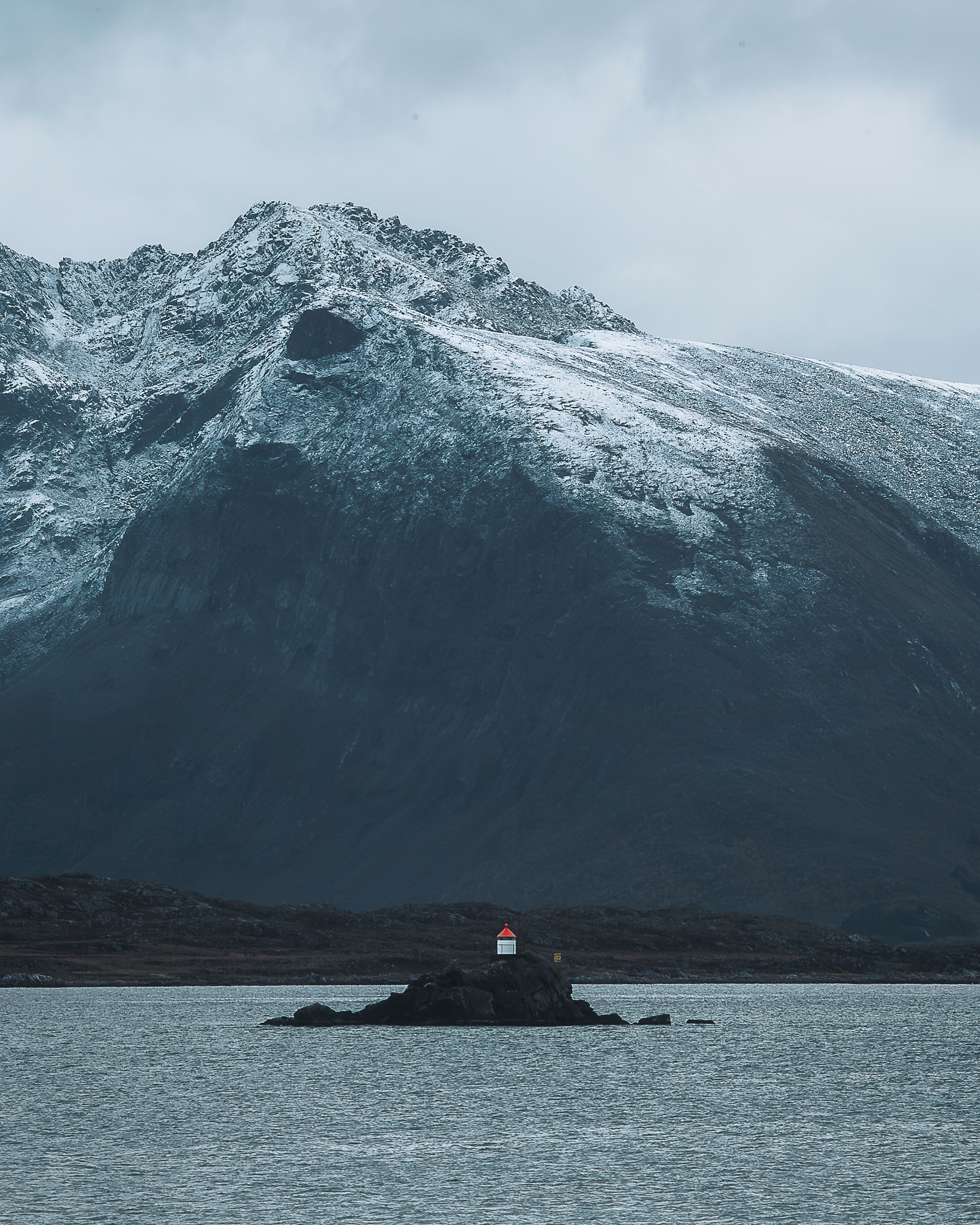 Fabrizio Casale captures a remote lighthouse on a small island beneath towering snow-covered mountains, conveying solitude and dramatic natural scale.