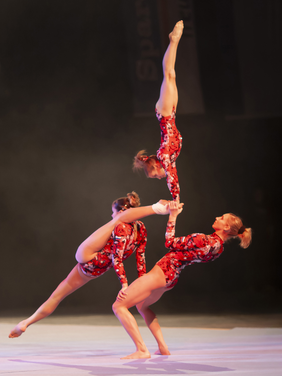 Three gymnasts performing an acrobatic lift on stage, showcasing movement and balance in street and sports photography.