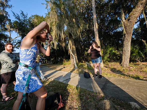 a person in a blue dress holds up a camera while others watch or pose