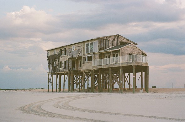 a run down stilt house stands on a white sand beach