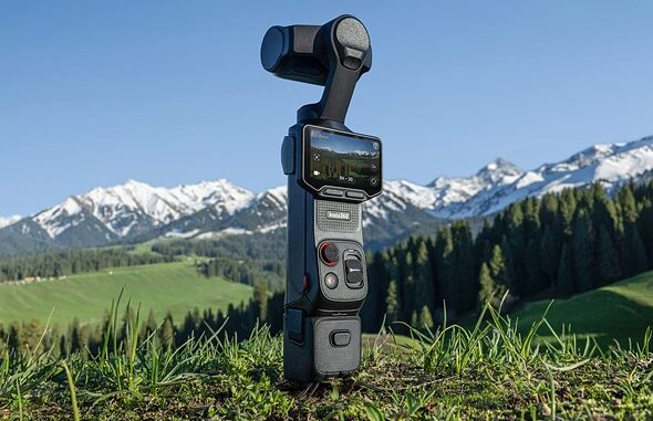 an_insta360_luna_ultra_camera_gimbal_stands_on_a_grassy_hill_in_front_of_snow_capped_mountains