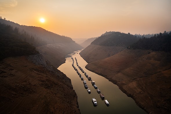 boats line a river in two neat rows with smoke filling the valley behind them