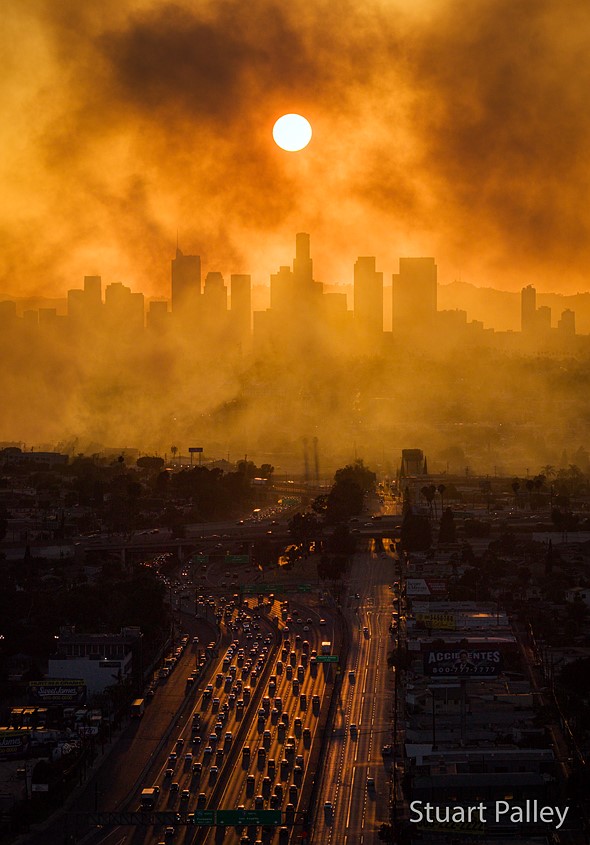 cars line a freeway that leads to a smoke covered cityscape