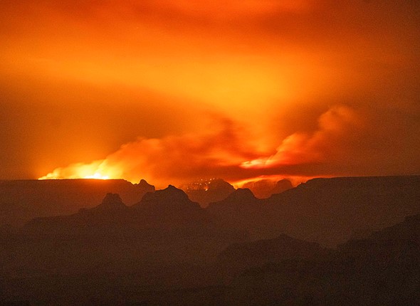 flames from a fire glow in the distance over mountain ridges with a sky glowing orange