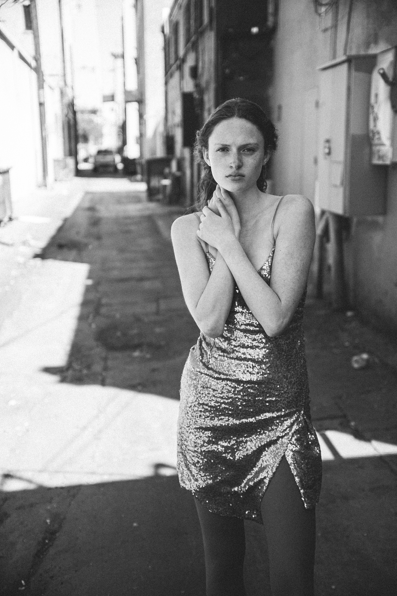 Black and white portrait by Holger Nitschke of a woman in a sequined dress standing in a sunlit urban alleyway.