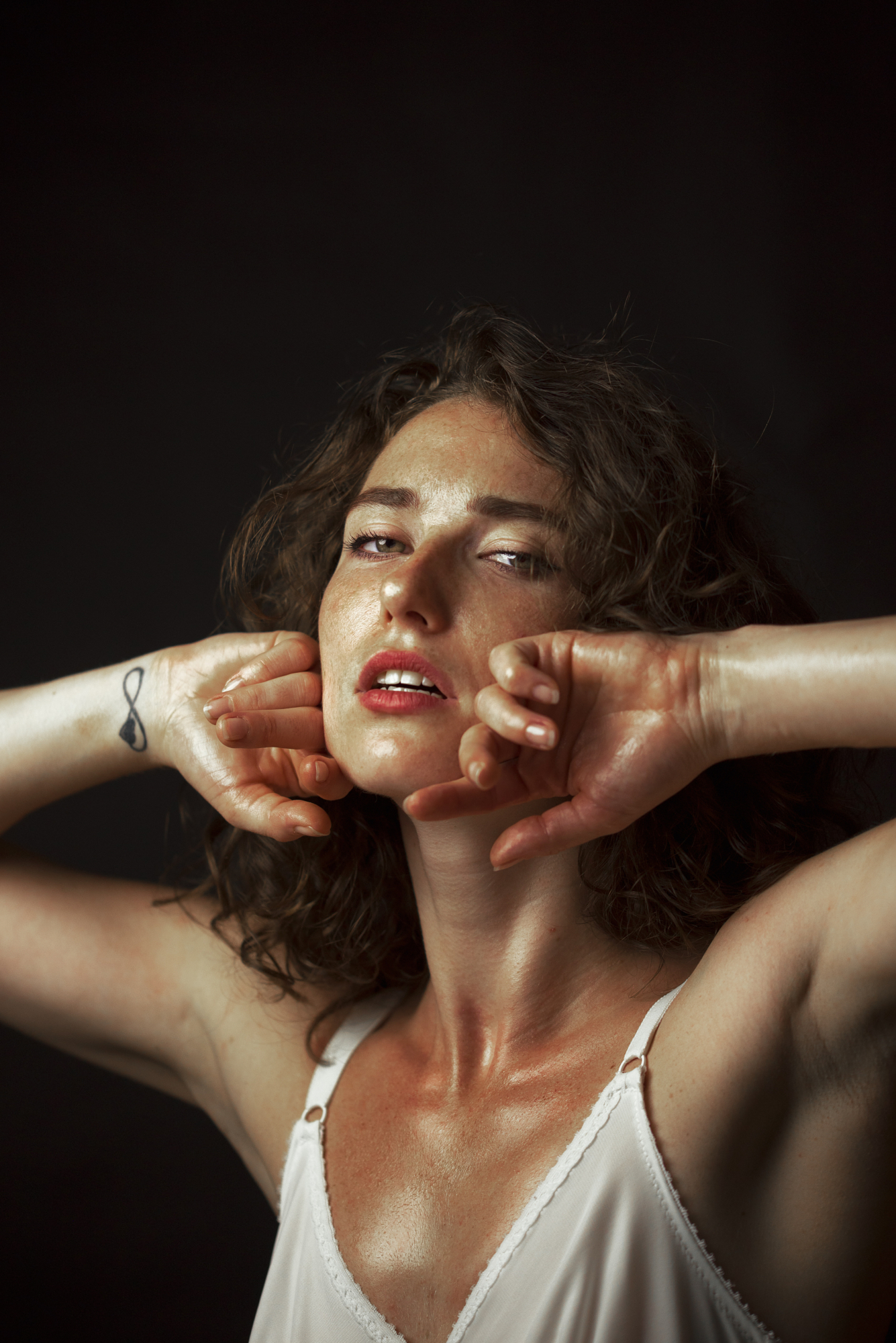 Dramatic fine art portrait with chiaroscuro lighting by Micaela Belgiorno photography showing a model with curly hair framed in light and deep shadow.