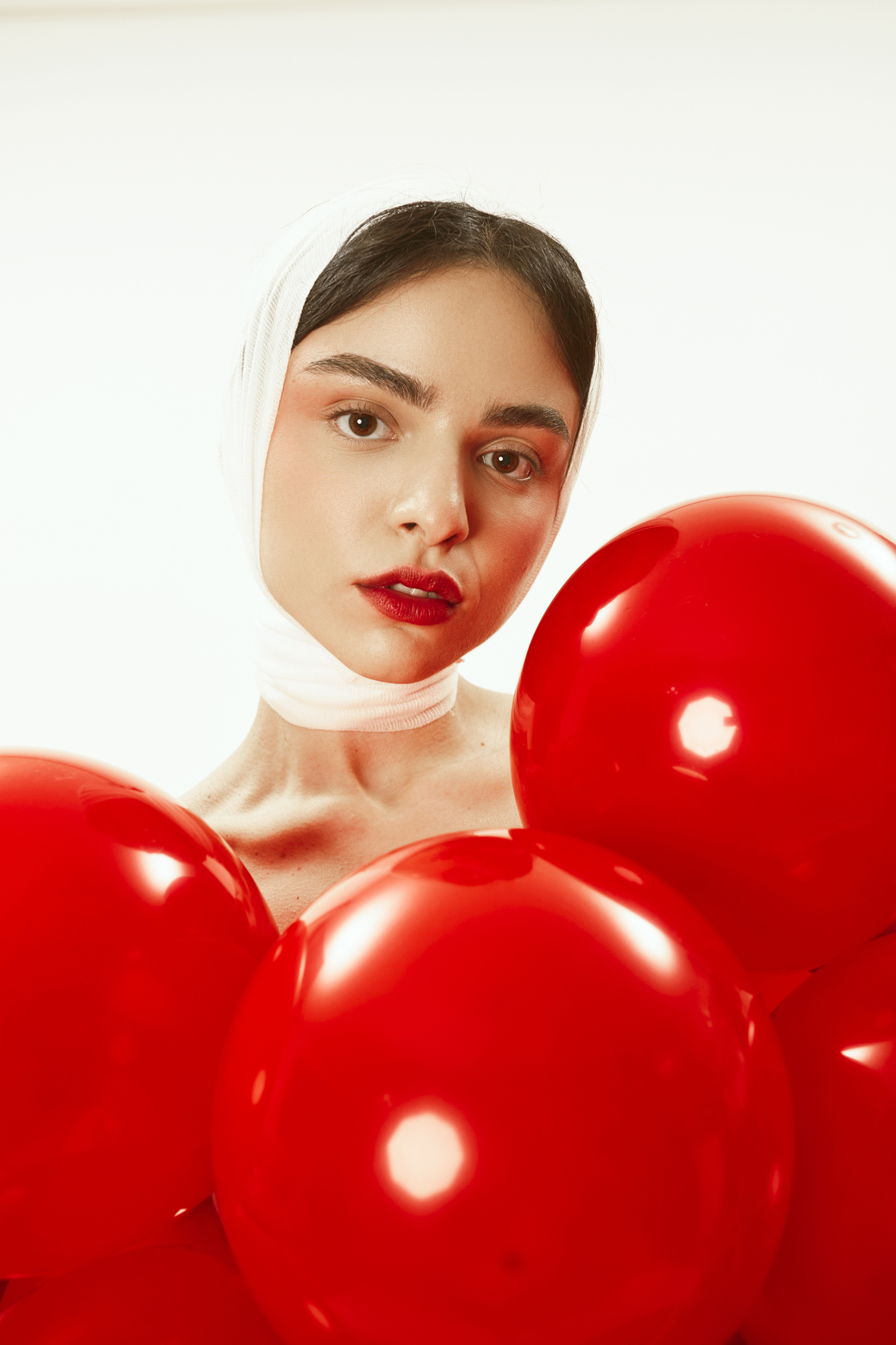 Bold editorial portrait featuring vibrant red balloons and tactile white head fabric styled by photographer Micaela Belgiorno.