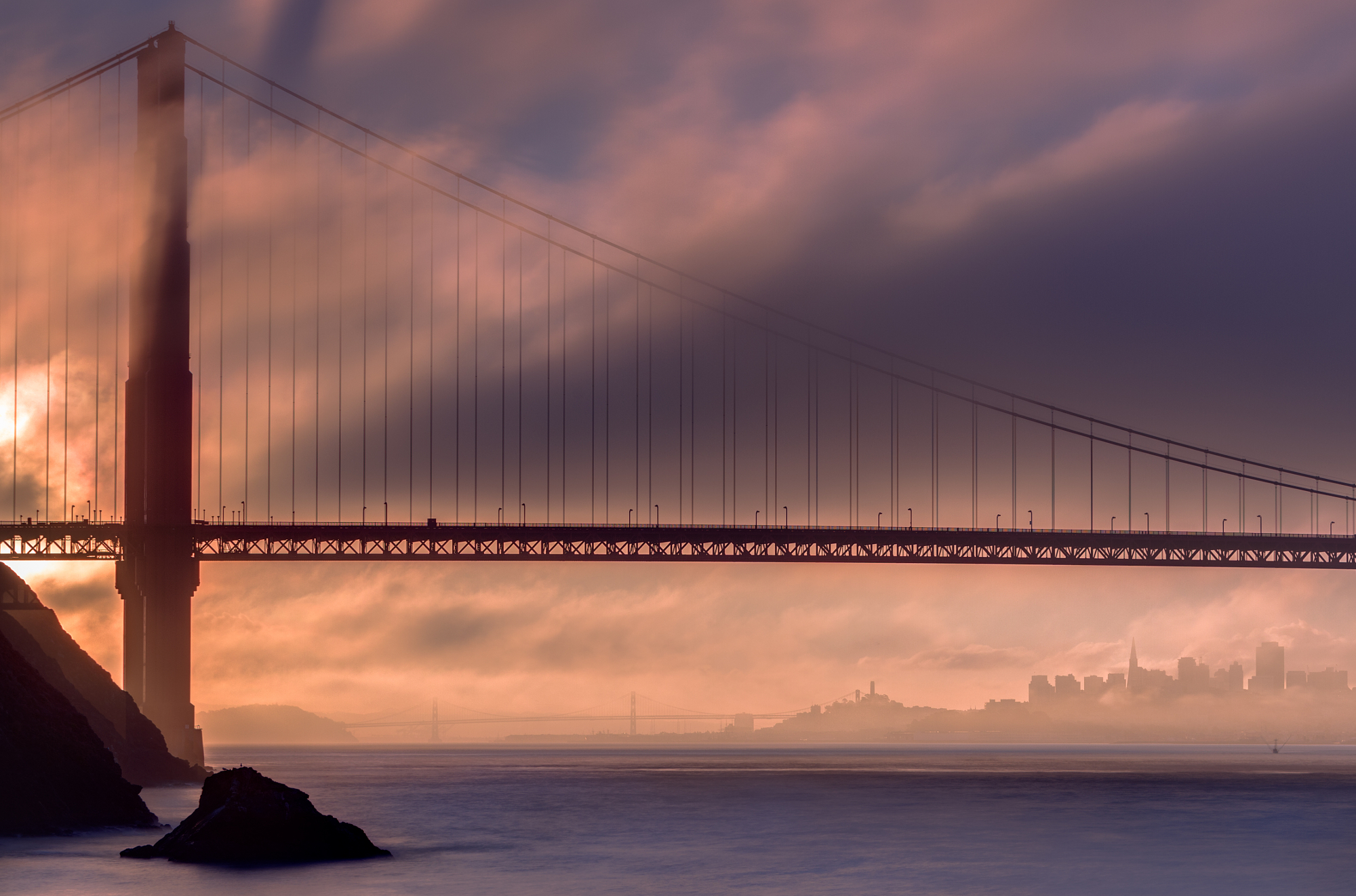 The Golden Gate Bridge enveloped in low-lying fog against a warm sunset sky, demonstrating classic landscape photography tips.