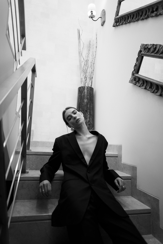 Black and white fashion portrait of a woman in a suit jacket on stairs, an example of David Velez photography.