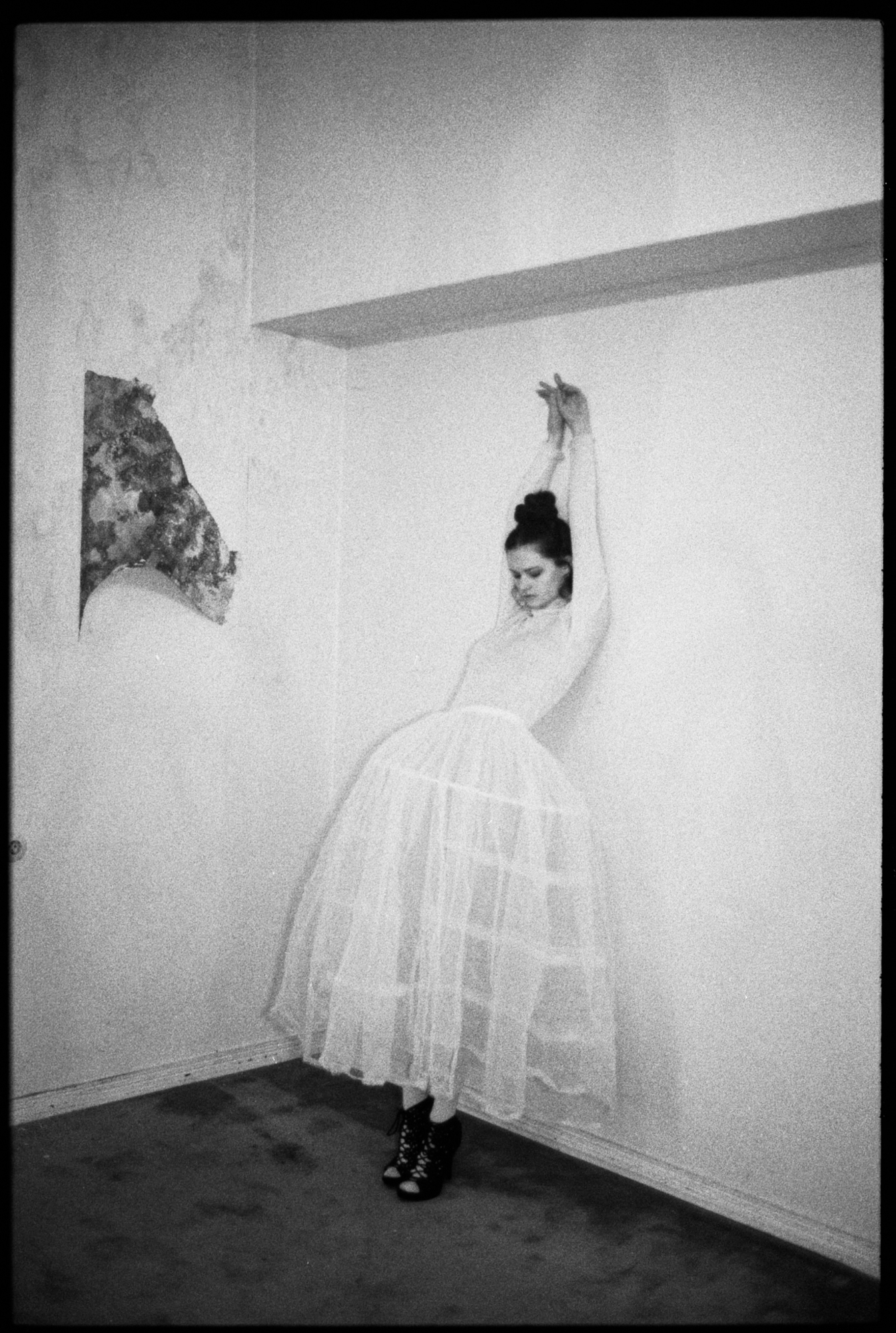 Minimalist black and white fashion portrait by Holger Nitschke featuring a woman in a white caged petticoat dress leaning against a wall.