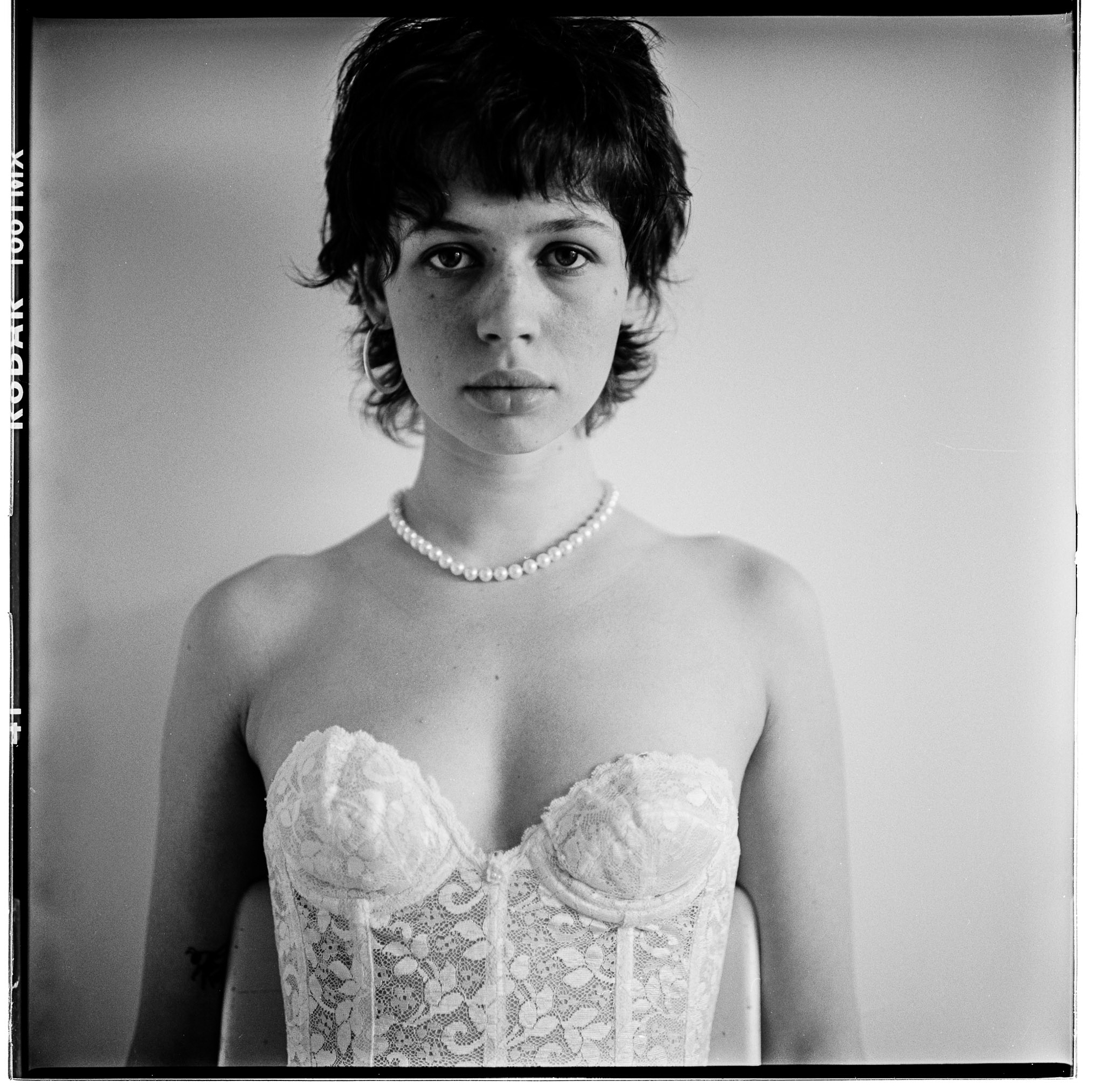 Kodak analog film black and white portrait by Holger Nitschke of a woman wearing a pearl necklace and white lace corset.