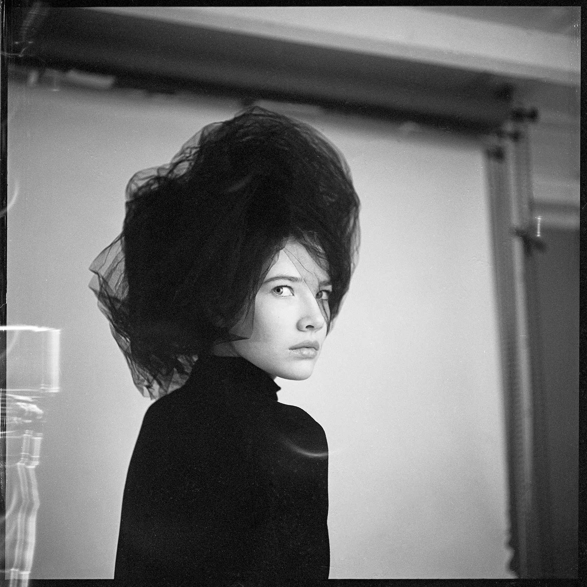 Studio black and white fashion portrait by Holger Nitschke showing a woman in a black turtleneck looking over her shoulder.