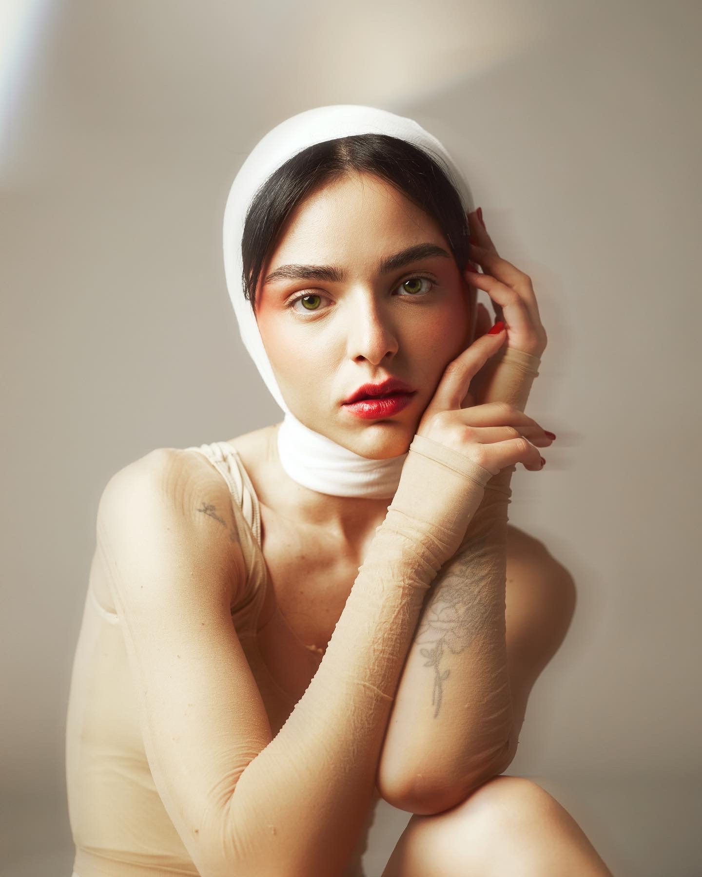 Introspective fine art fashion portrait by Micaela Belgiorno photography featuring a young woman with a white fabric headwrap, sheer nude sleeves, and soft editorial portrait lighting.