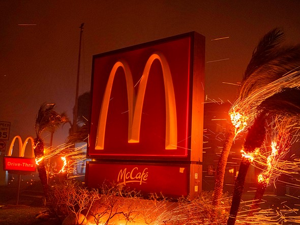 sparks fly from burning palm trees around a mcdonalds sign at night