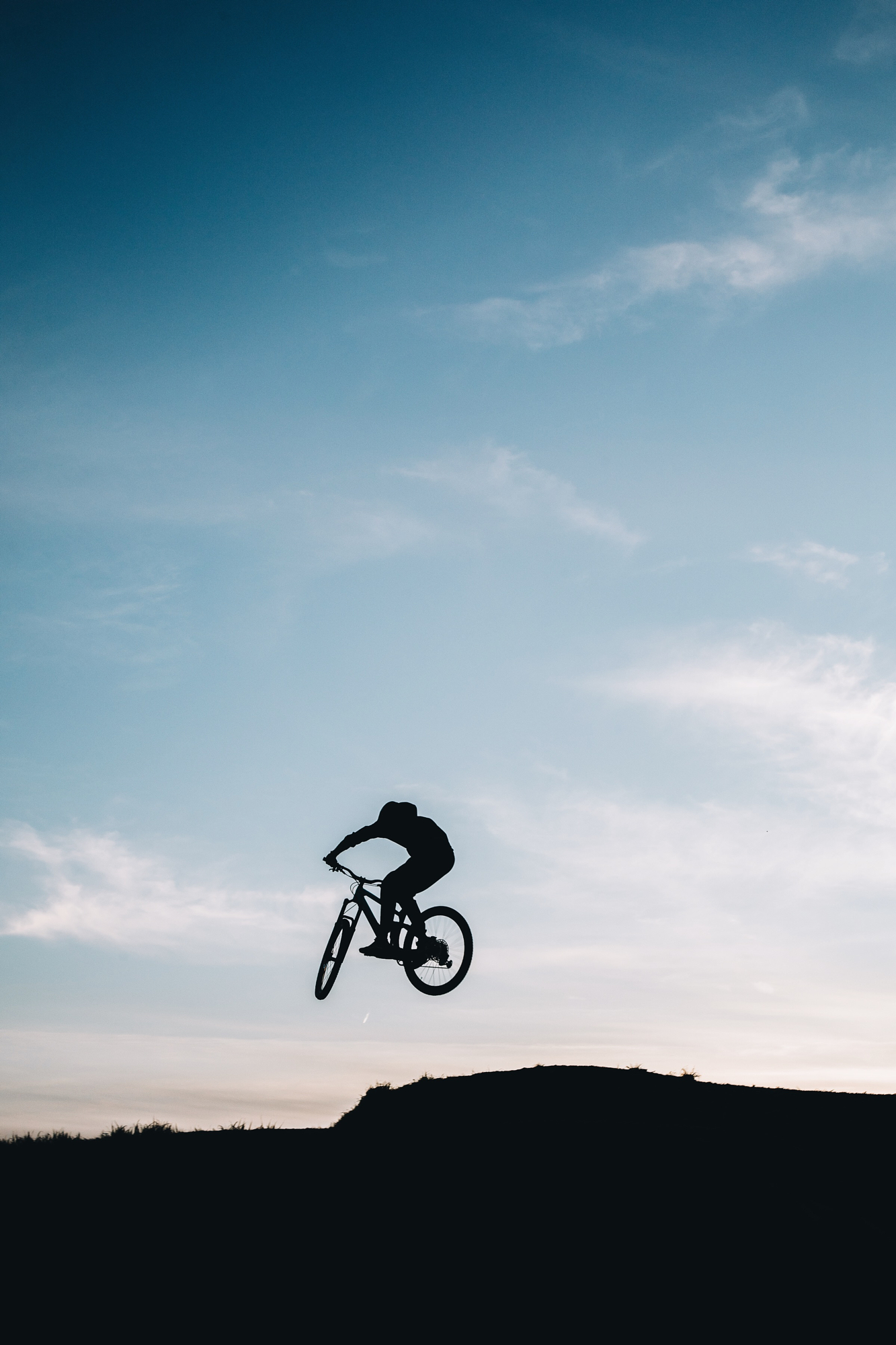 Airborne mountain biker silhouette captured against a bright sky using backlight photography techniques.