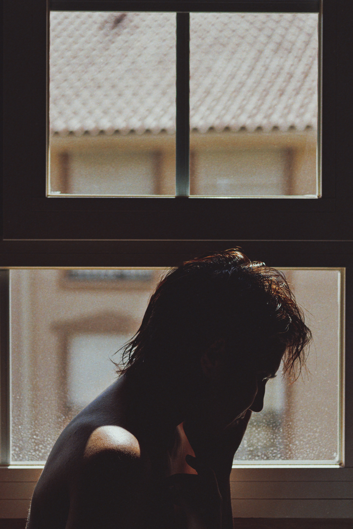Indoor portrait silhouette of a young woman looking down, backlit by a bright window.