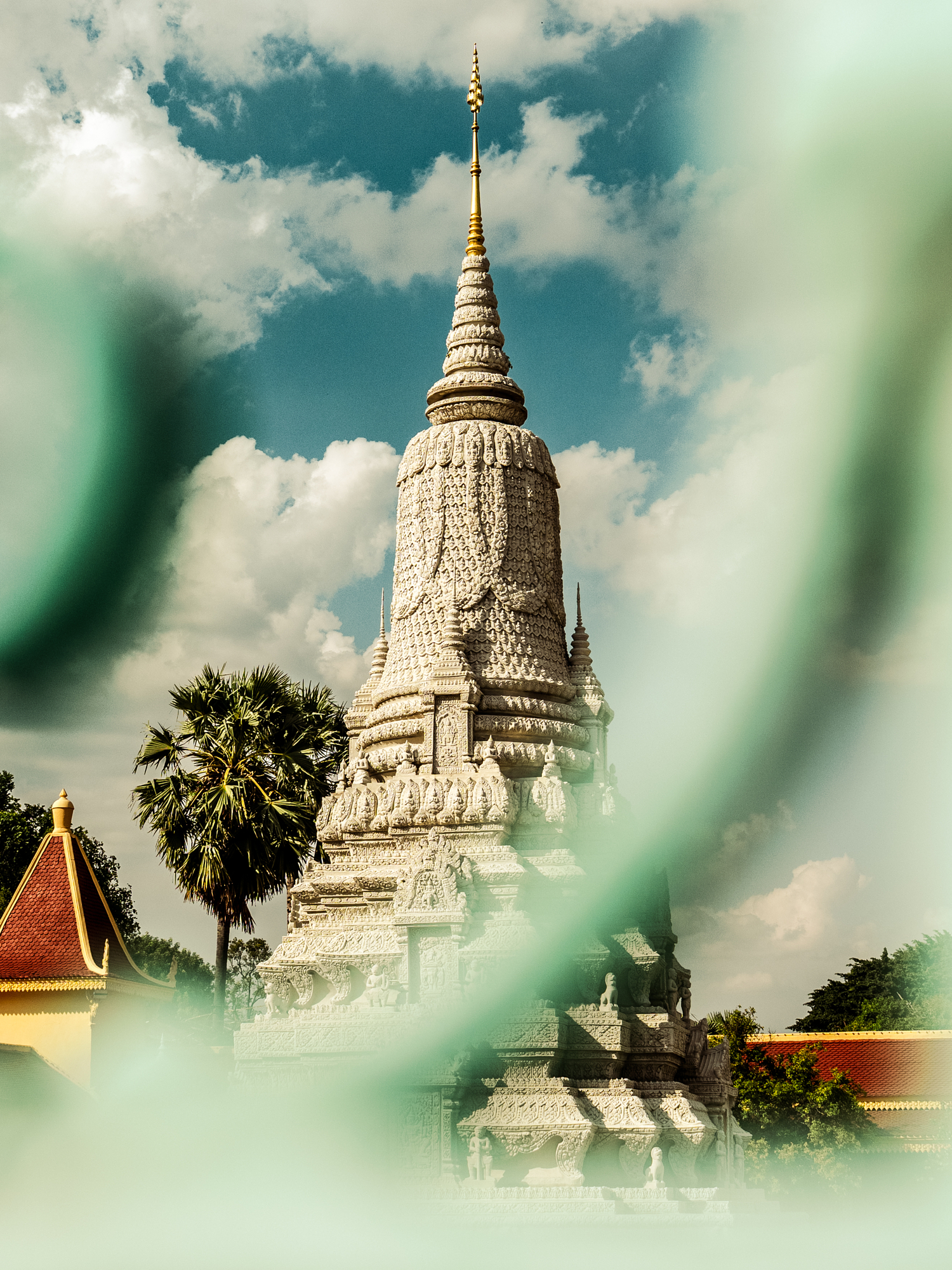 Ornate white Cambodian stupa seen through a soft screen of green foliage