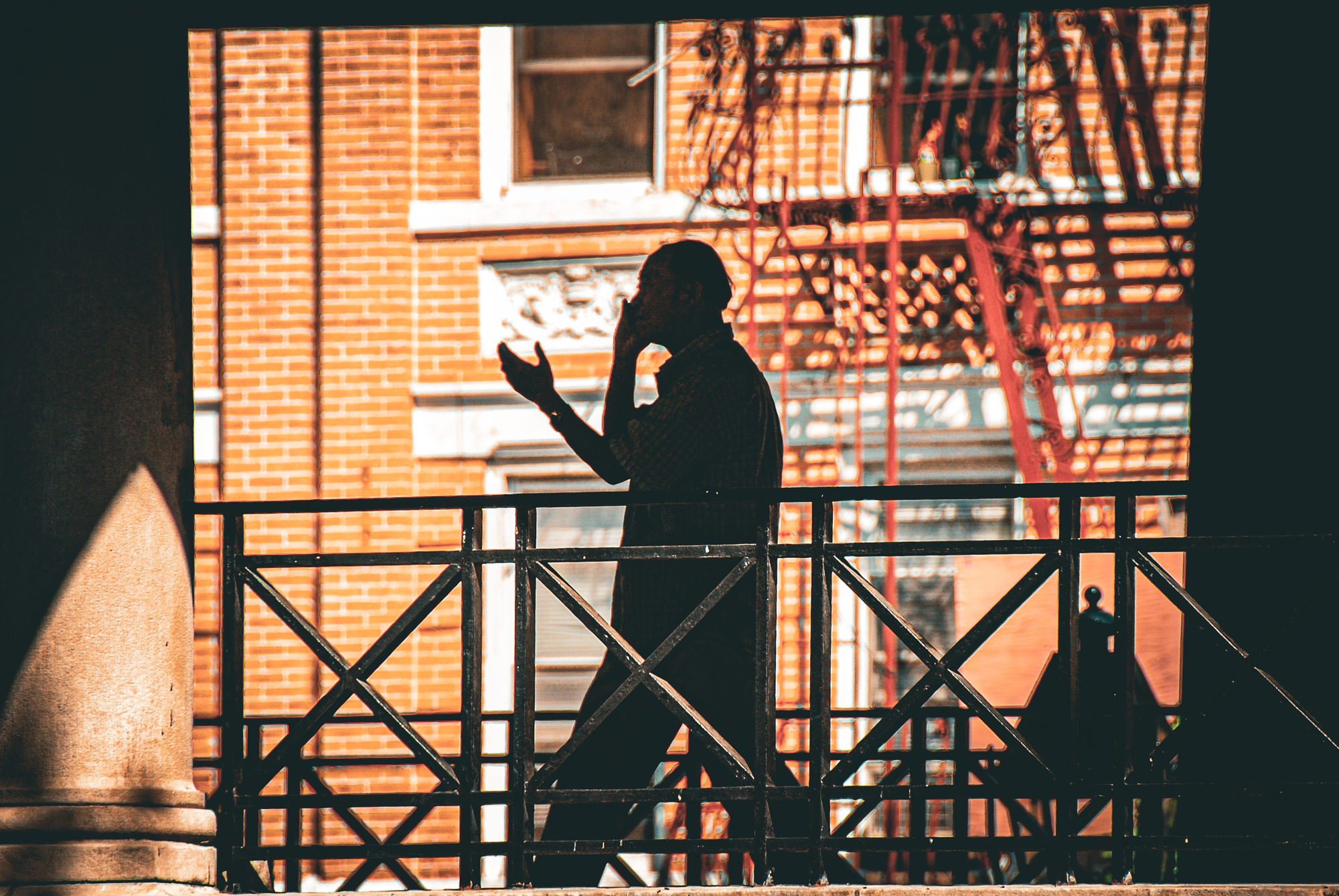 Silhouette of a man on the phone against a sunlit brick facade and fire escape