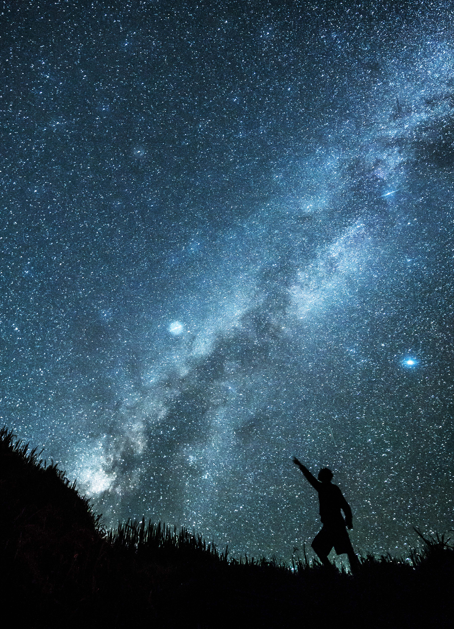 Silhouette of a person reaching towards the brilliant blue Milky Way star field at night, astrophotography by Gonzalo Bendito