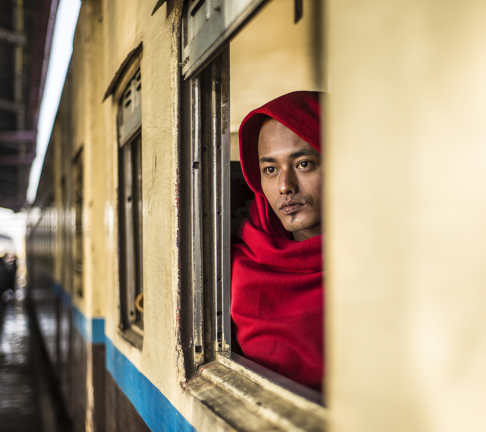 Documentary travel portrait of a man in a red hood looking out of a train window by Gonzalo Bendito