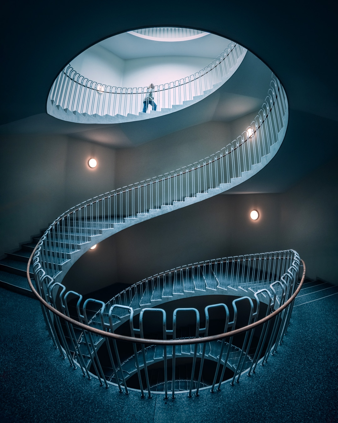 Spiral staircase curving through a blue-lit stairwell in a long S shape