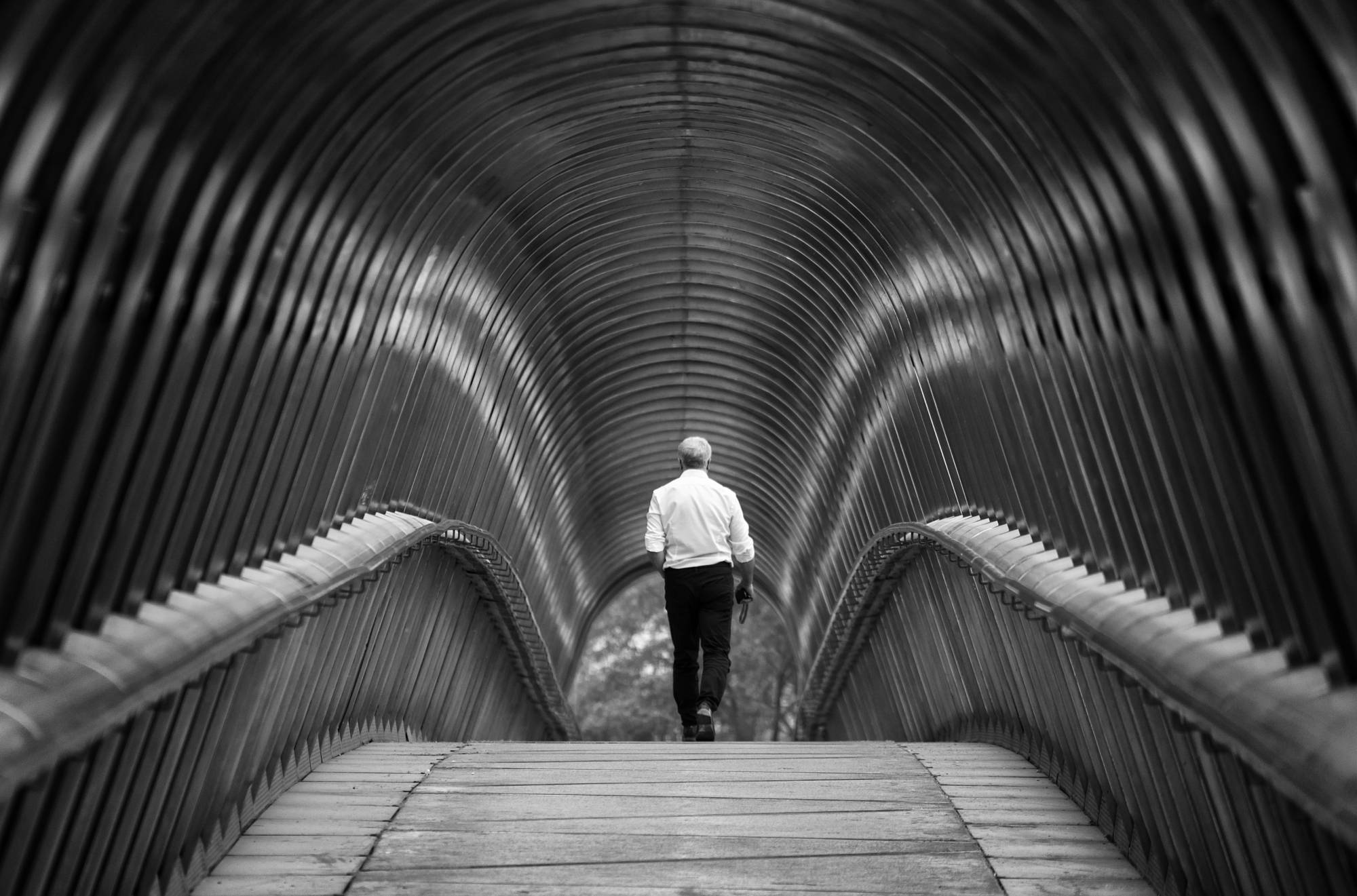 Man walking alone through a ribbed metal footbridge in black and white